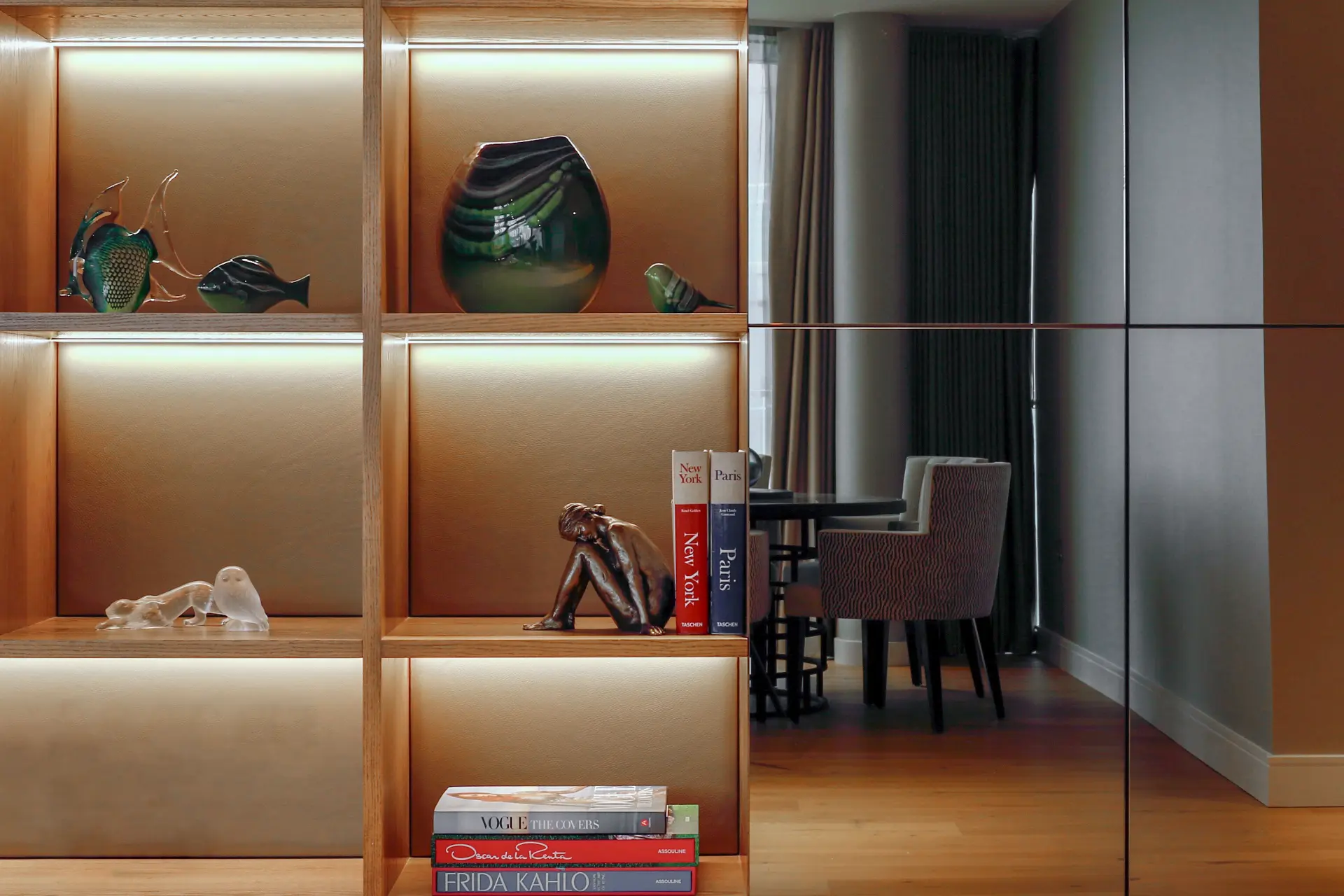 Bespoke artisan detail — illuminated oak and leather shelving with a bronze figure, hand-blown glass ornaments and collected objects